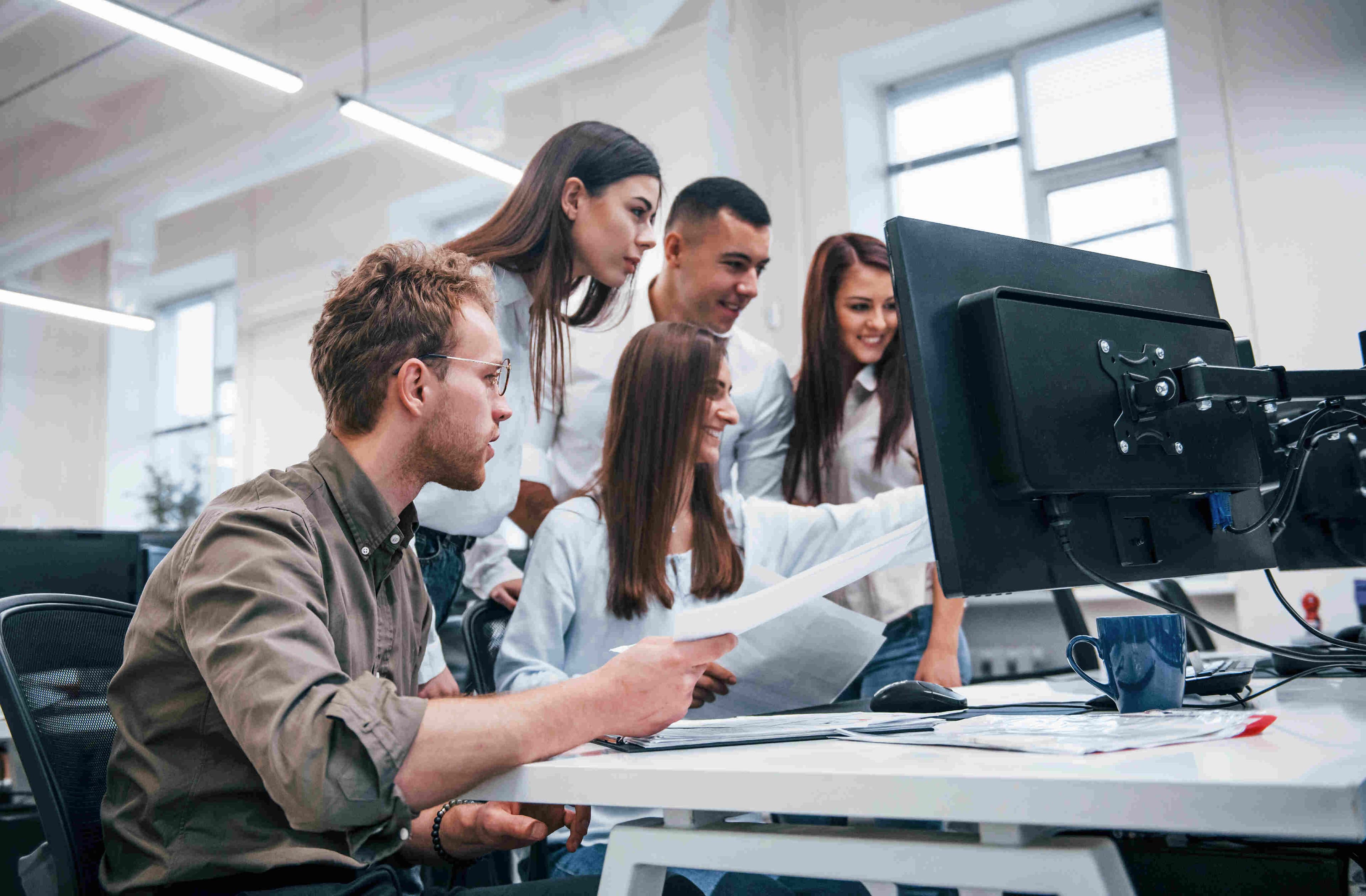 A team of young professionals sharing ideas and joyfully discussing project details at a computer.