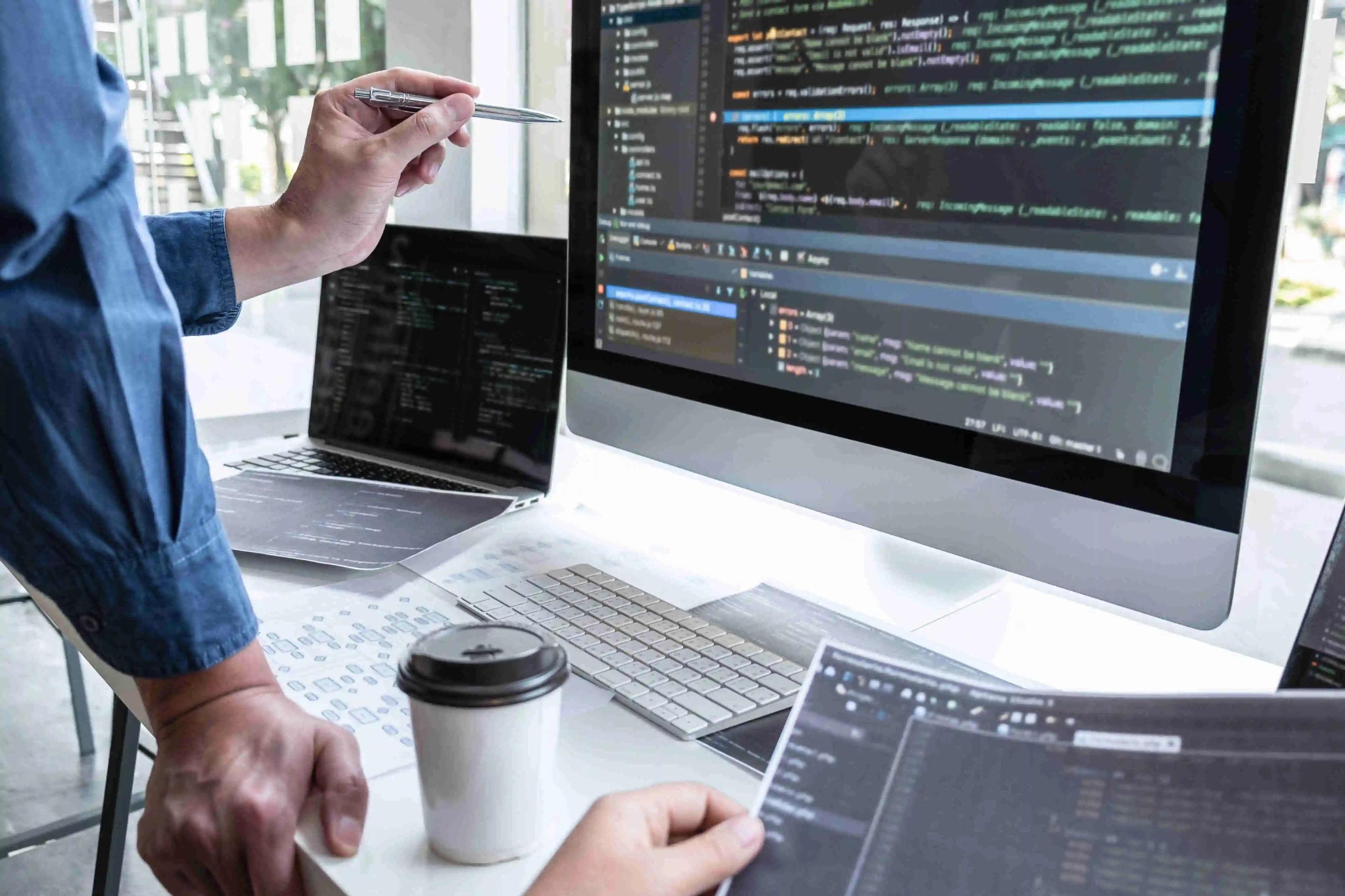 Team of programmers collaborating on a project, with a hand holding a pen pointing at the screen, suggesting active discussion and brainstorming.